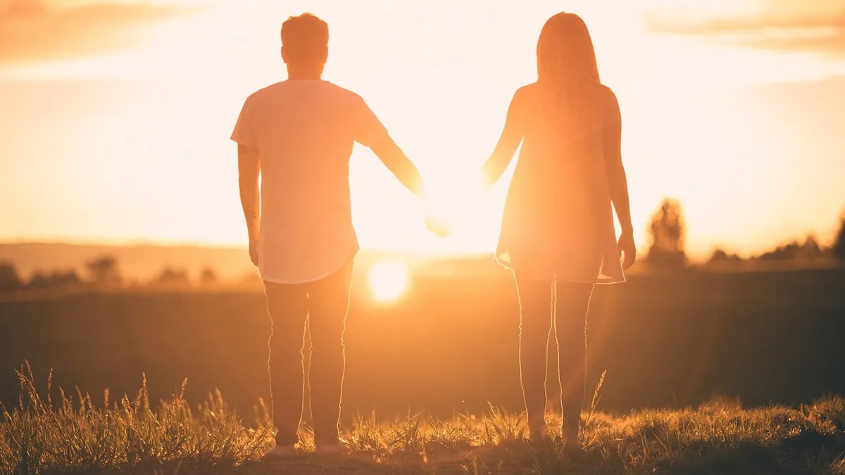 Couple holding hands while walking through a field at sunset